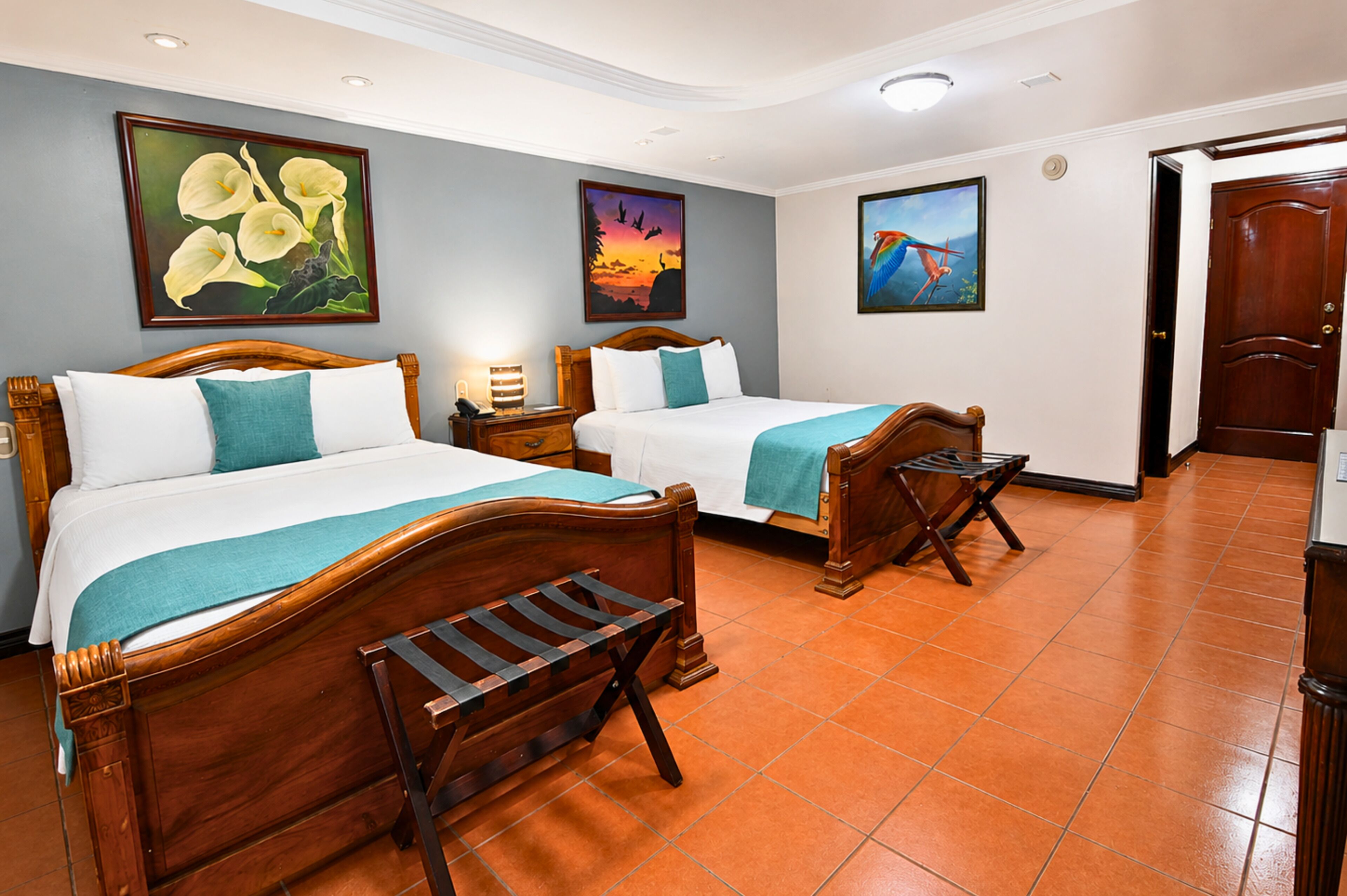 A hotel room with two wooden beds, a nightstand, a bench, and artwork on the walls.