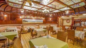 Un restaurante con paneles de madera, manteles verdes, sillas de mimbre y un cuadro grande en la pared.