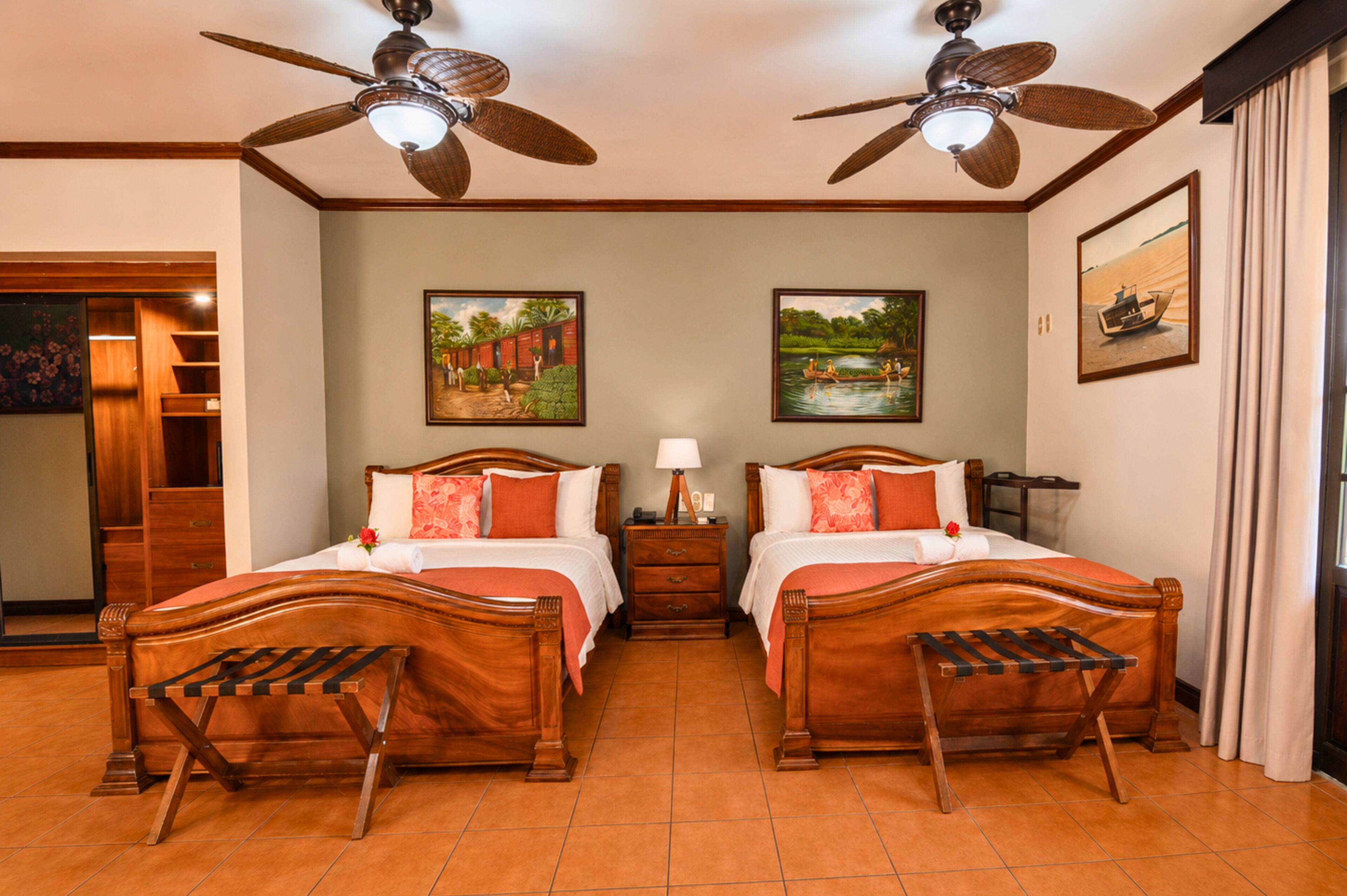 A hotel room with two wooden beds, a nightstand, a ceiling fan, and artwork on the walls.