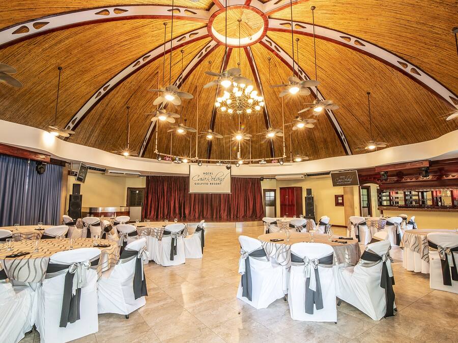 A large hall with round tables and chairs, a wooden ceiling, and a chandelier.