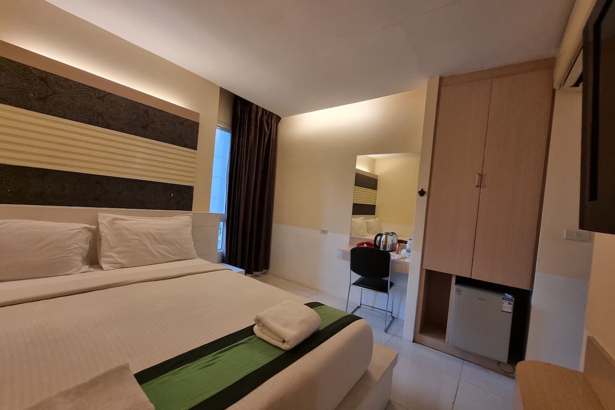 A hotel room with a large bed, a desk, a wardrobe, and a mirror.