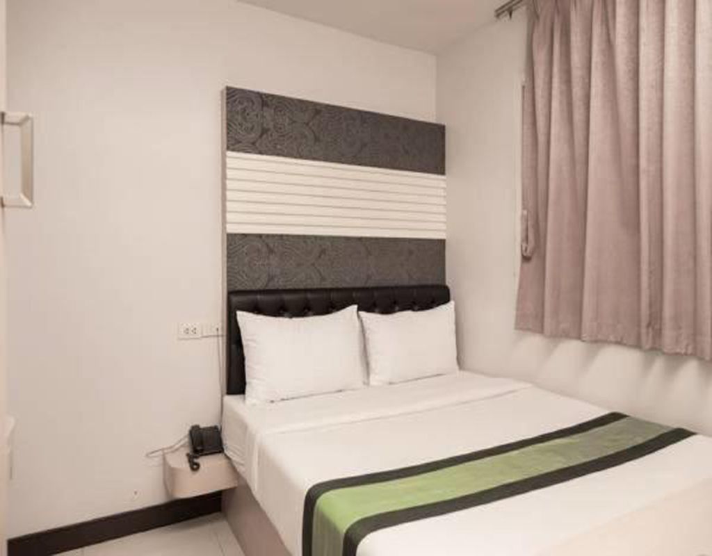 A hotel room with a bed, a headboard, a bedside table, and a window with curtains.