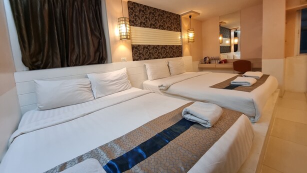 Habitación de hotel con dos camas, un espejo grande, una mesita de noche con artículos de aseo y una ventana con cortinas.
