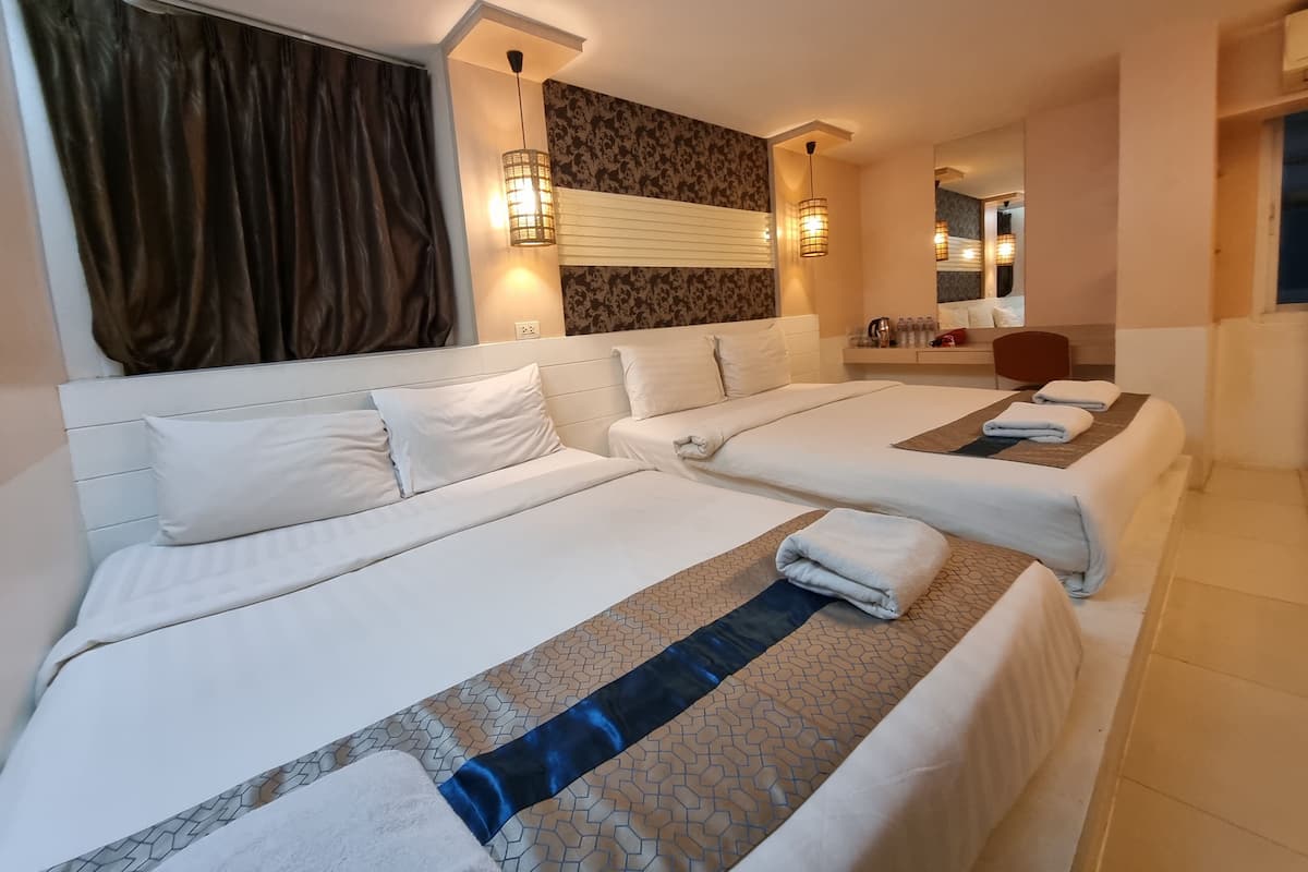 A hotel room with two beds, a large mirror, a bedside table with toiletries, and a window with curtains.