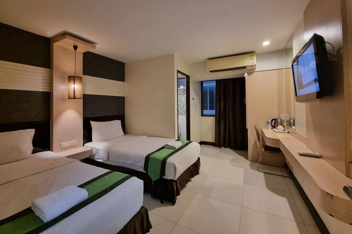 Habitación de hotel con dos camas, un escritorio, un televisor y un equipo de aire acondicionado.