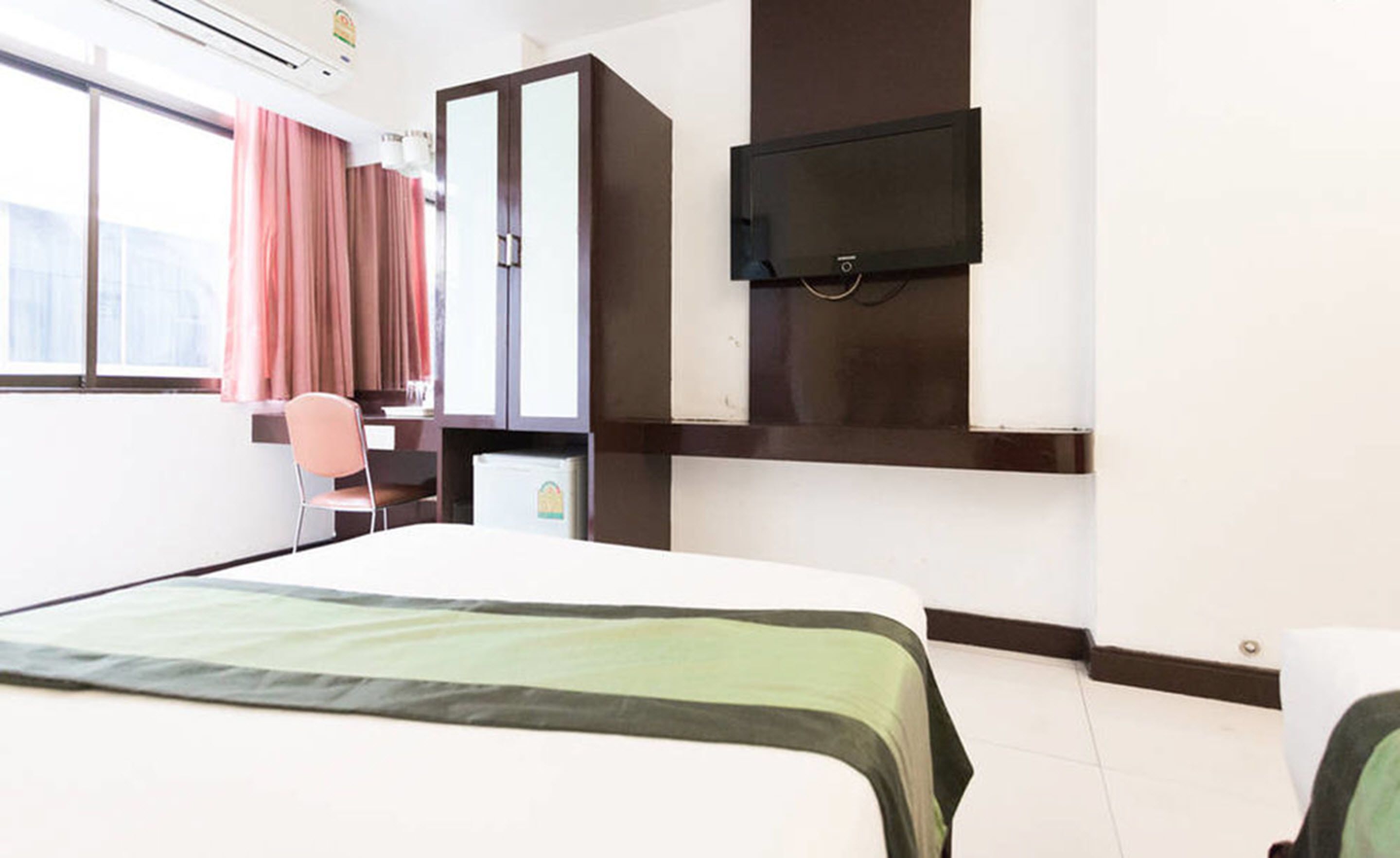 Una habitación de hotel con cama, escritorio, silla, televisor y ventana con cortinas.
