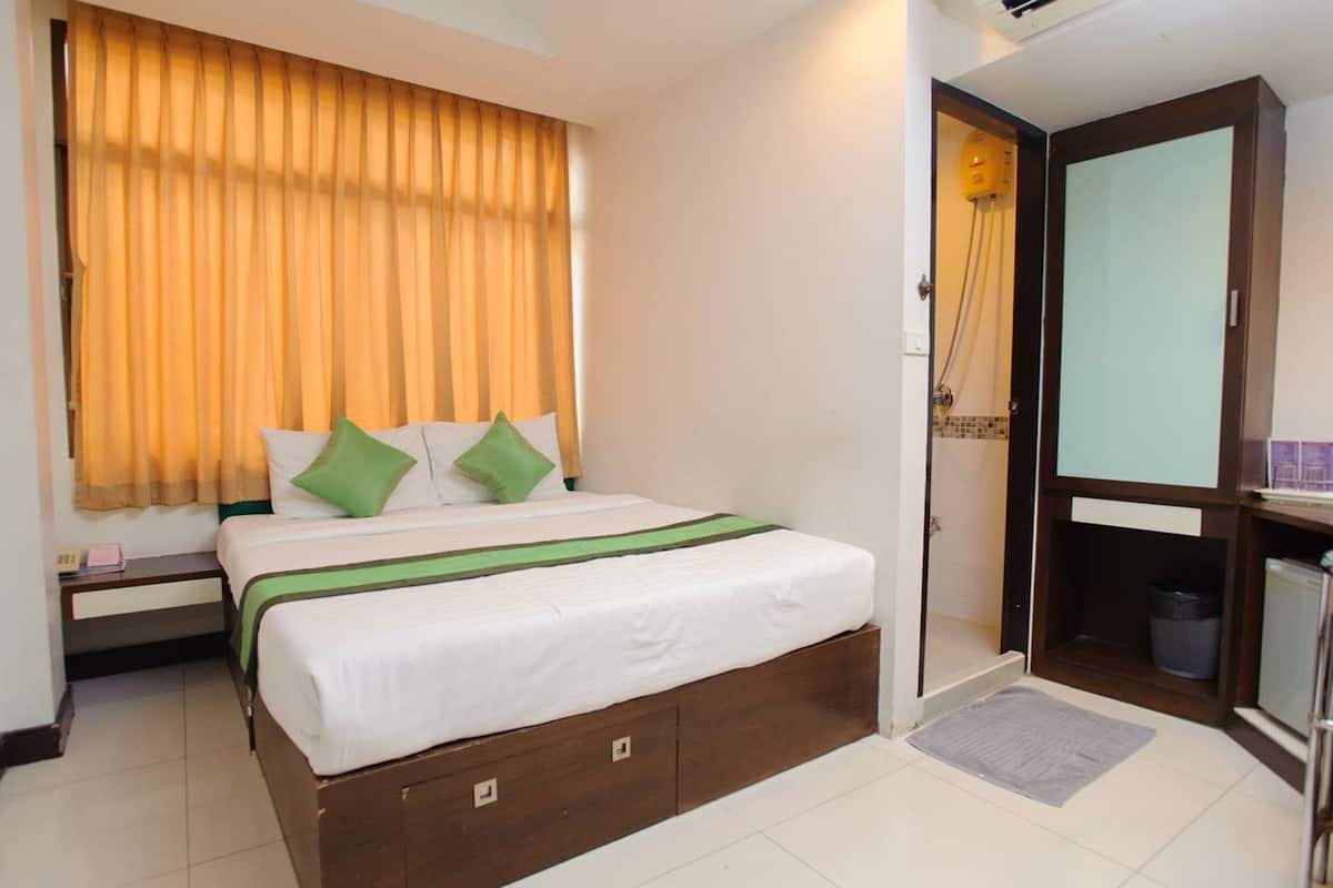 Habitación de hotel con cama, mesita de noche, espejo, puerta que da a un balcón y un pequeño cubo de basura.