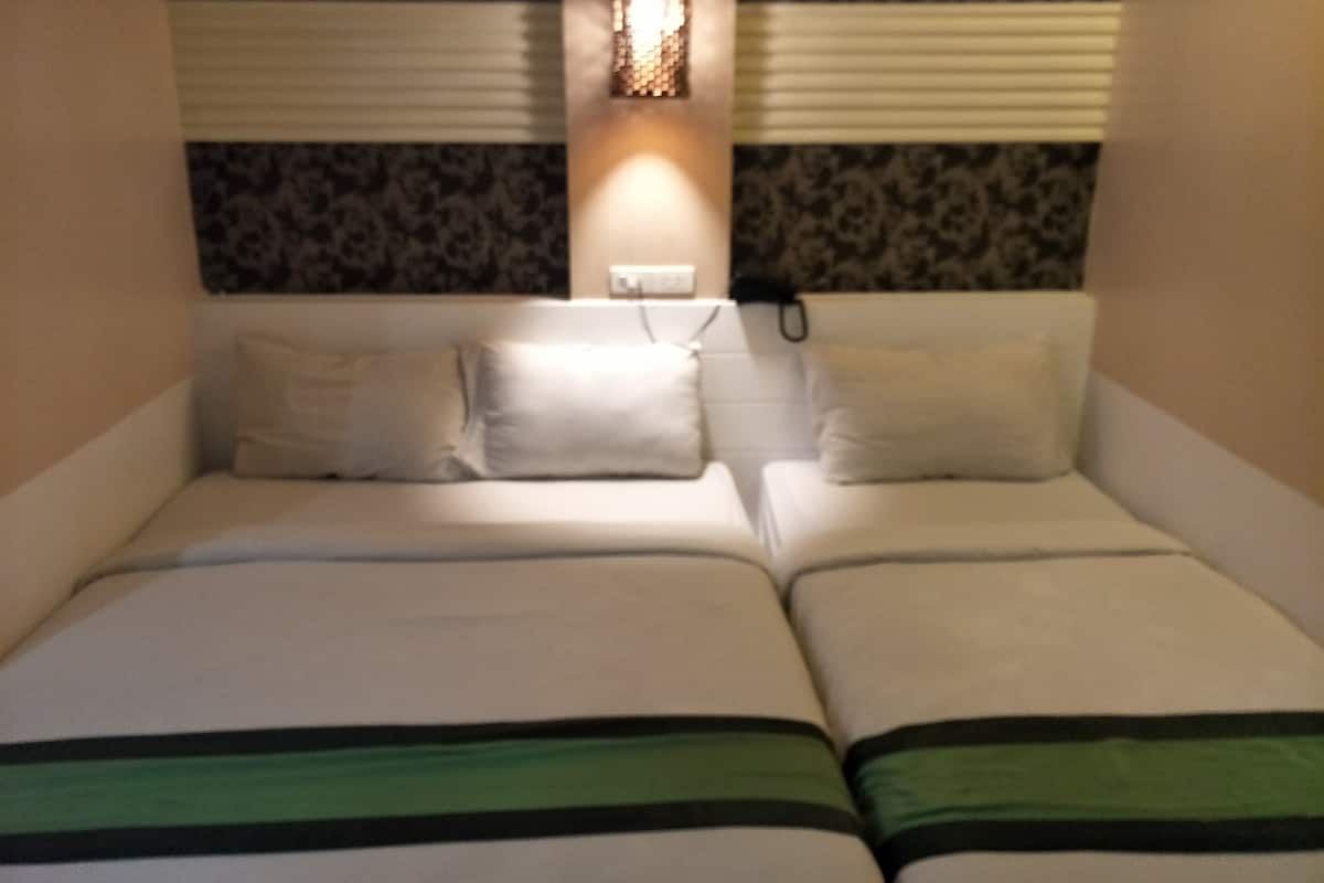 A double bed with white bedding and green stripes, a wall-mounted light fixture, and a power outlet.