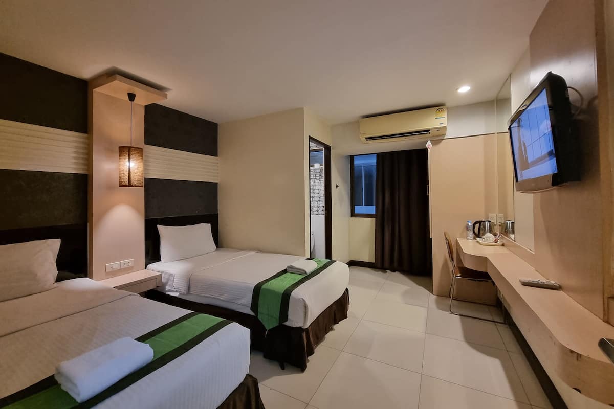 A hotel room with two beds, a desk, a television, and an air conditioning unit.