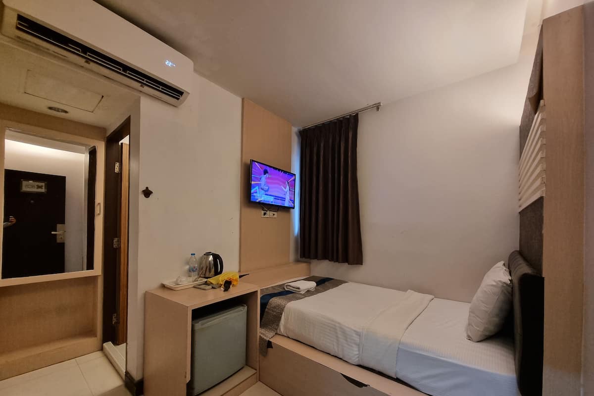 A compact hotel room with a bed, a small desk with a television, a mini-fridge, and a door leading to another room.