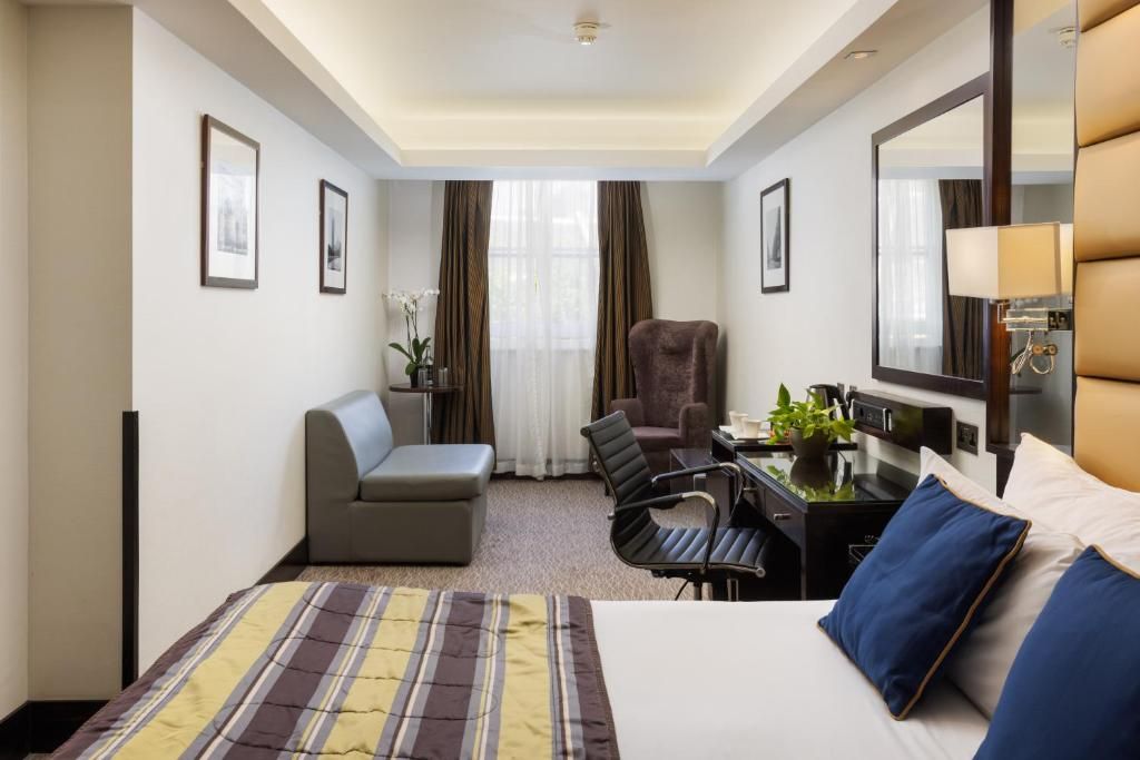 A hotel room with a bed, a desk with a computer, a chair, a sofa, and a large mirror.