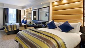 A hotel room with two beds, a desk, a chair, a mirror, and a window with curtains. - Park Grand Mayfair (London)