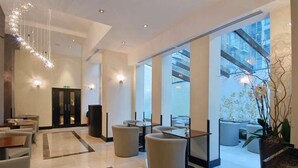 A modern lobby with a high ceiling, a chandelier, seating areas, and large windows offering views of the city. - Park Grand Mayfair (London)