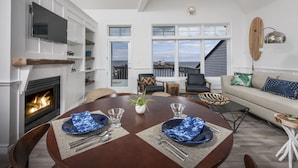 A dining area with a fireplace, a round table set for two, and a view of the ocean through large windows. - ViewPoint Hotel (York Beach)