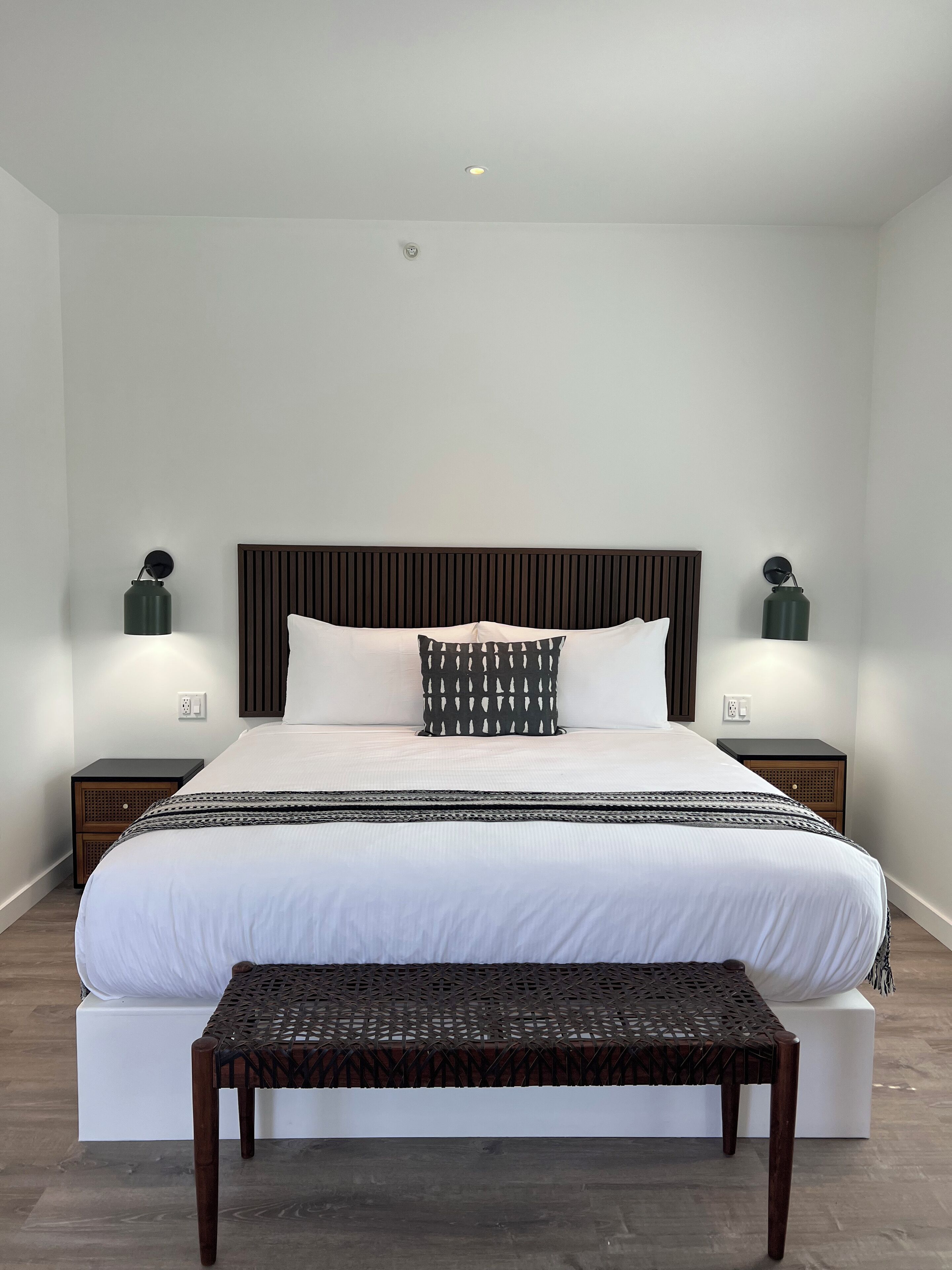 A modern bedroom with a large bed, two bedside tables, a bench, and two wall-mounted lamps.