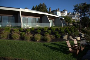 A modern house with large windows, a sloped roof, and a well-maintained garden with rocks and shrubs.
