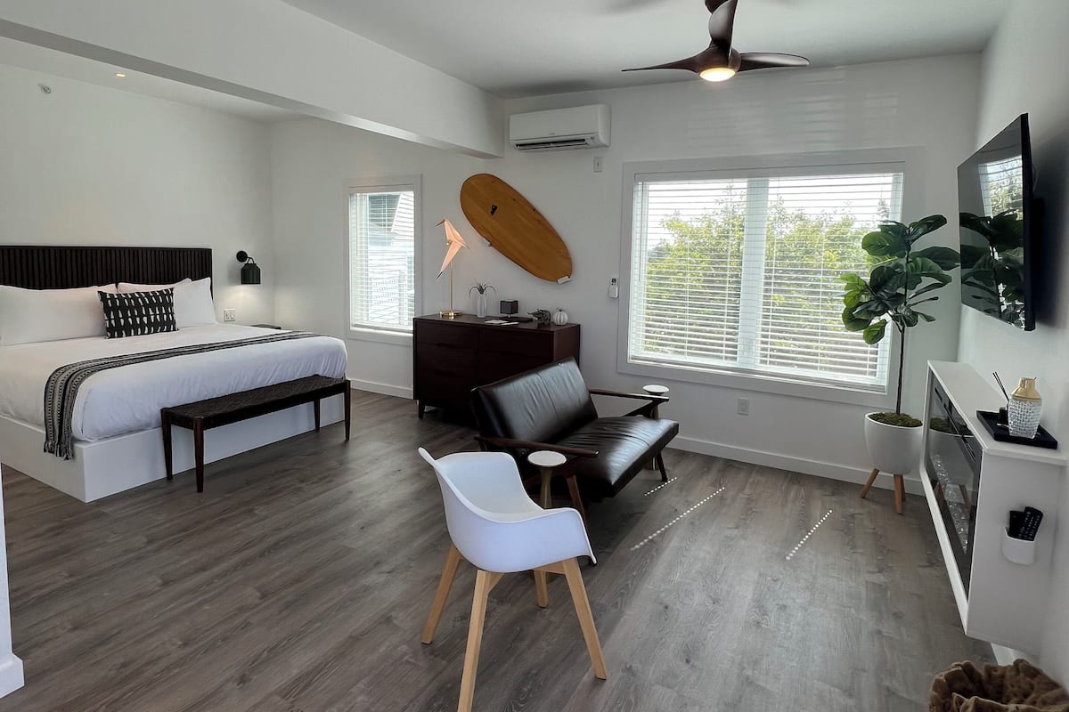 A modern bedroom with a bed, a desk, a chair, and a surfboard on the wall.