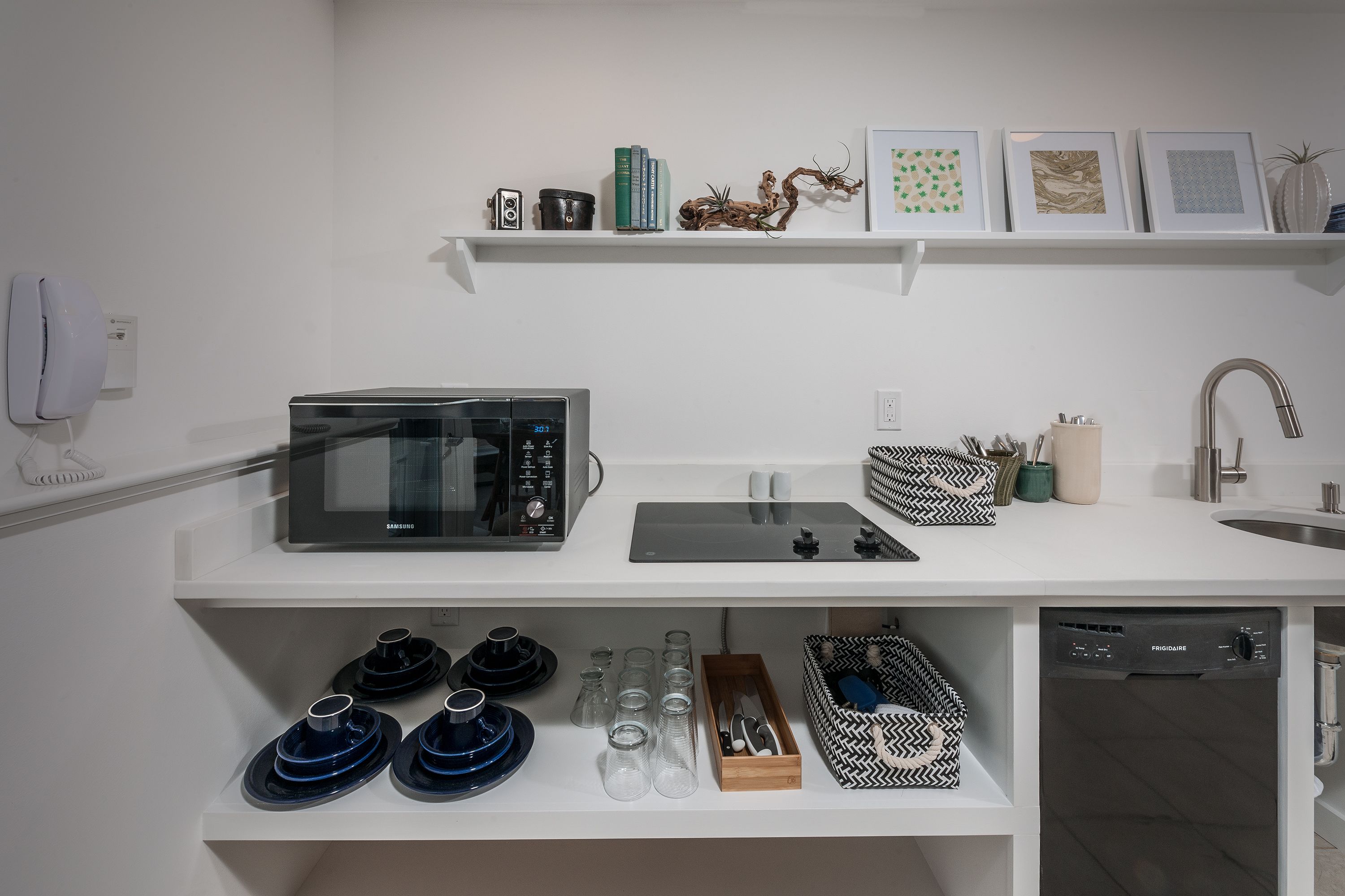 A modern kitchen with a microwave, toaster, and dishwasher. There are shelves with books, decorative items, and kitchenware.