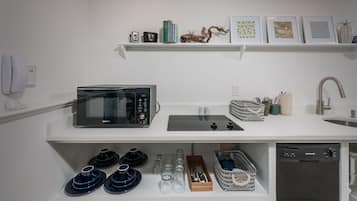 A modern kitchen with a microwave, toaster, and dishwasher. There are shelves with books, decorative items, and kitchenware.