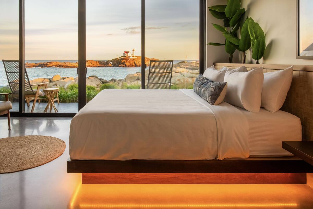 A bedroom with a large bed, a view of the sea, and a chair by the window.