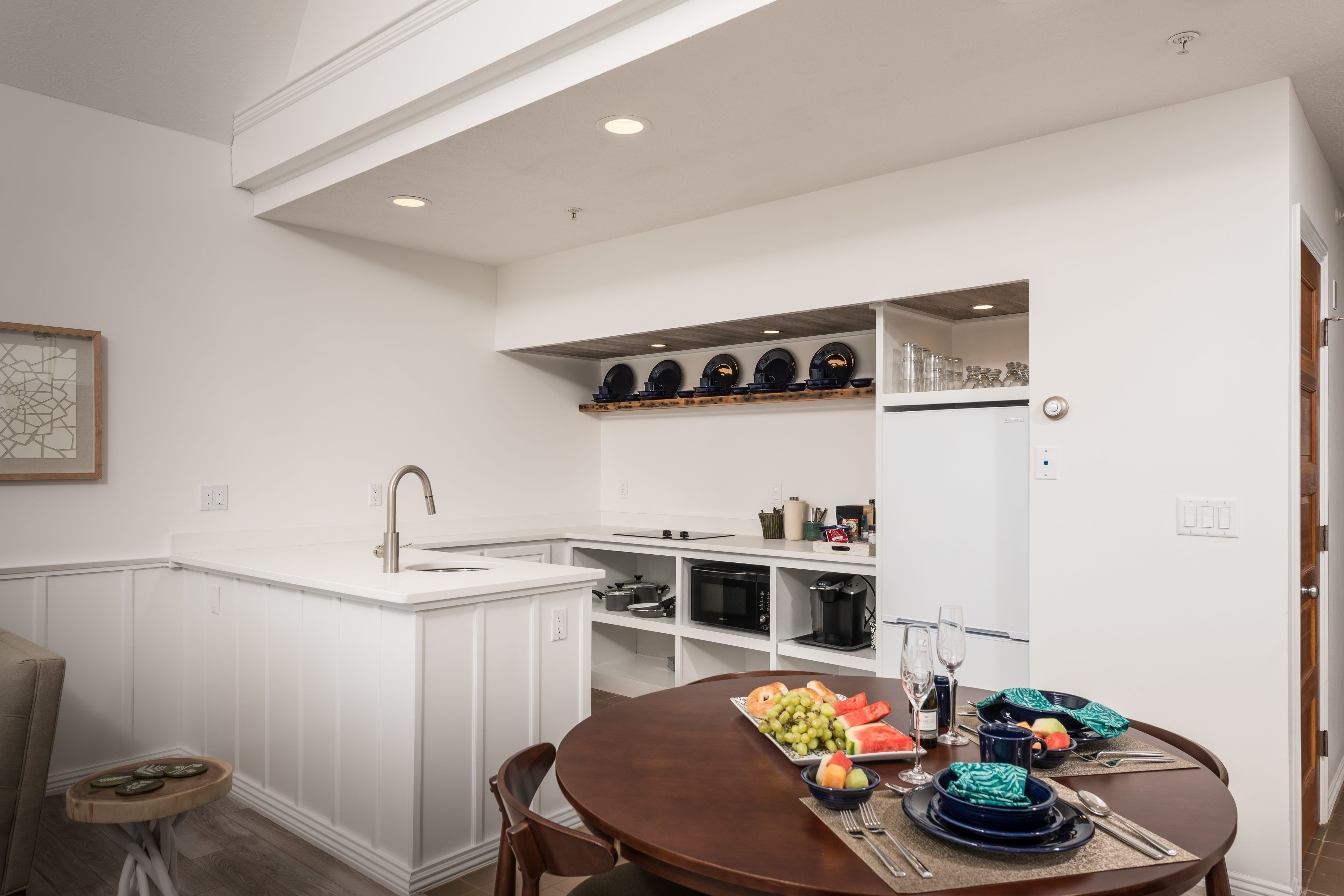 A modern kitchen with white cabinetry, a built-in microwave, and a dining area with a round table set for four.