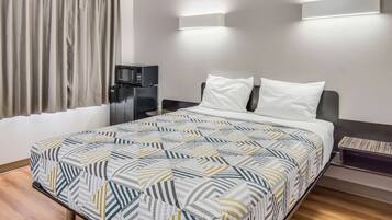 Una habitación de hotel con cama, mesita de noche, microondas e iluminación montada en la pared.