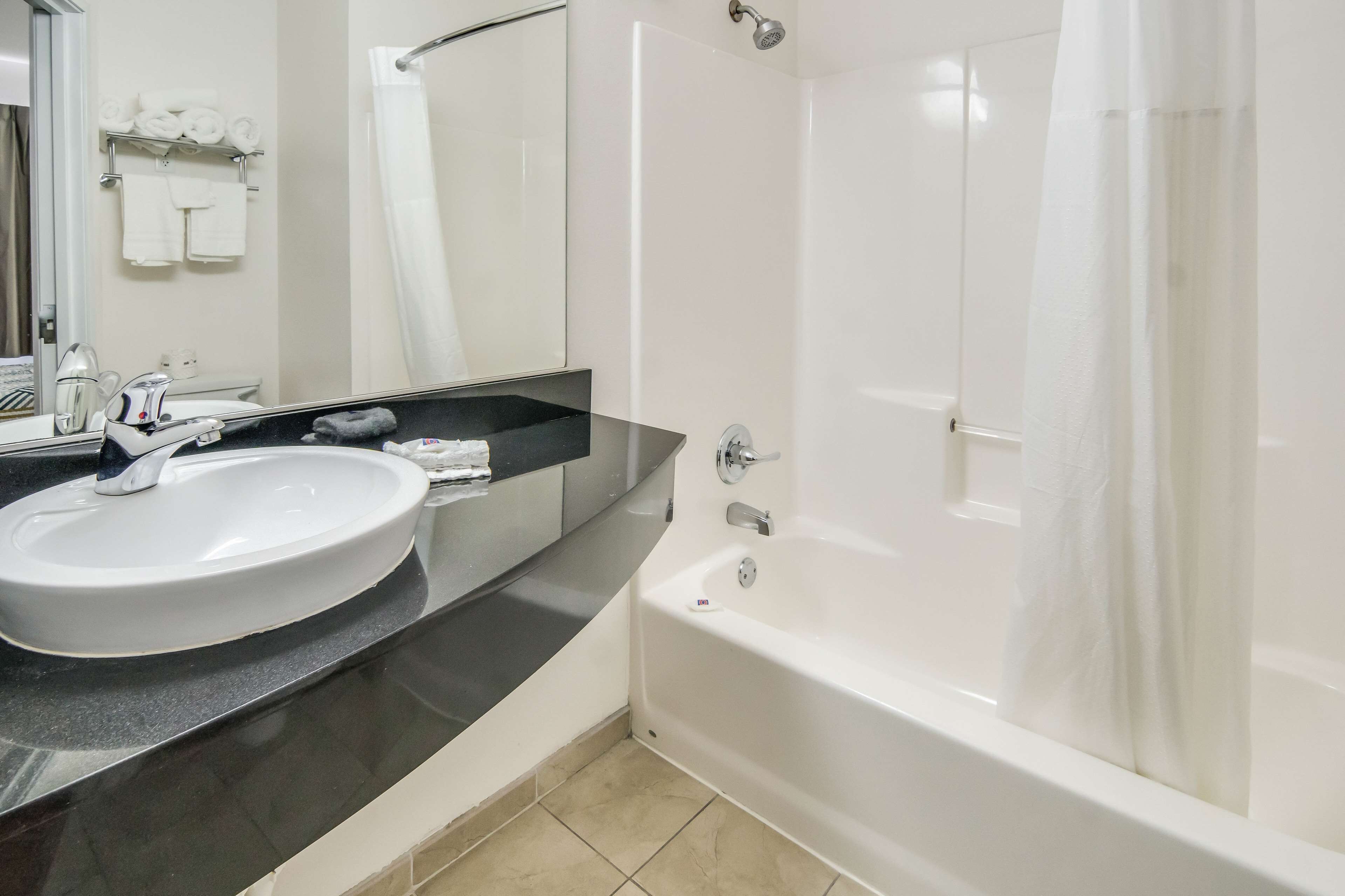 Un baño moderno con un lavamanos blanco, encimera negra y bañera blanca.
