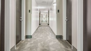 Un pasillo largo y estrecho con puertas a ambos lados, piso alfombrado e iluminación empotrada en el techo.