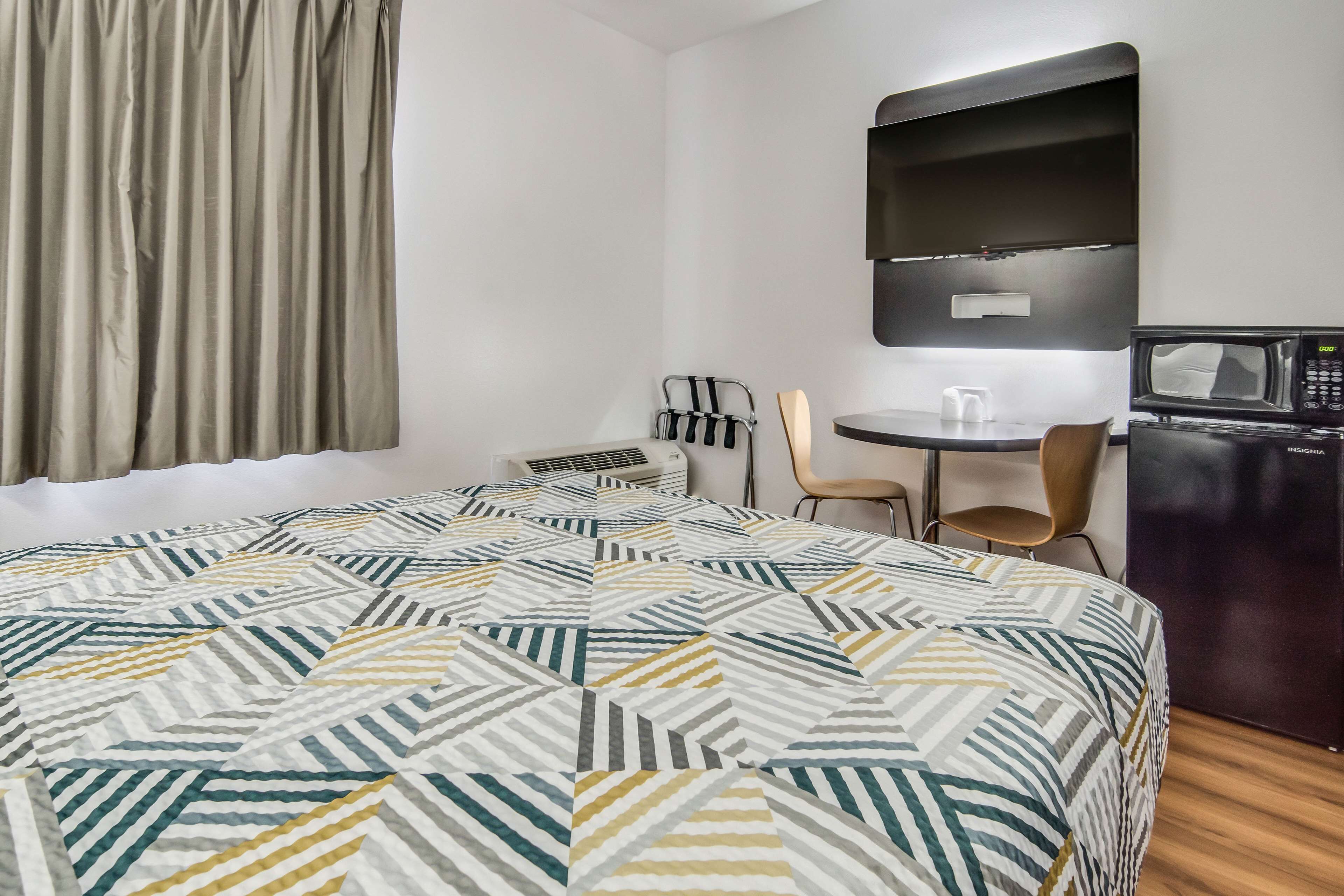 Habitación de hotel con cama, escritorio, silla, microondas y refrigerador.