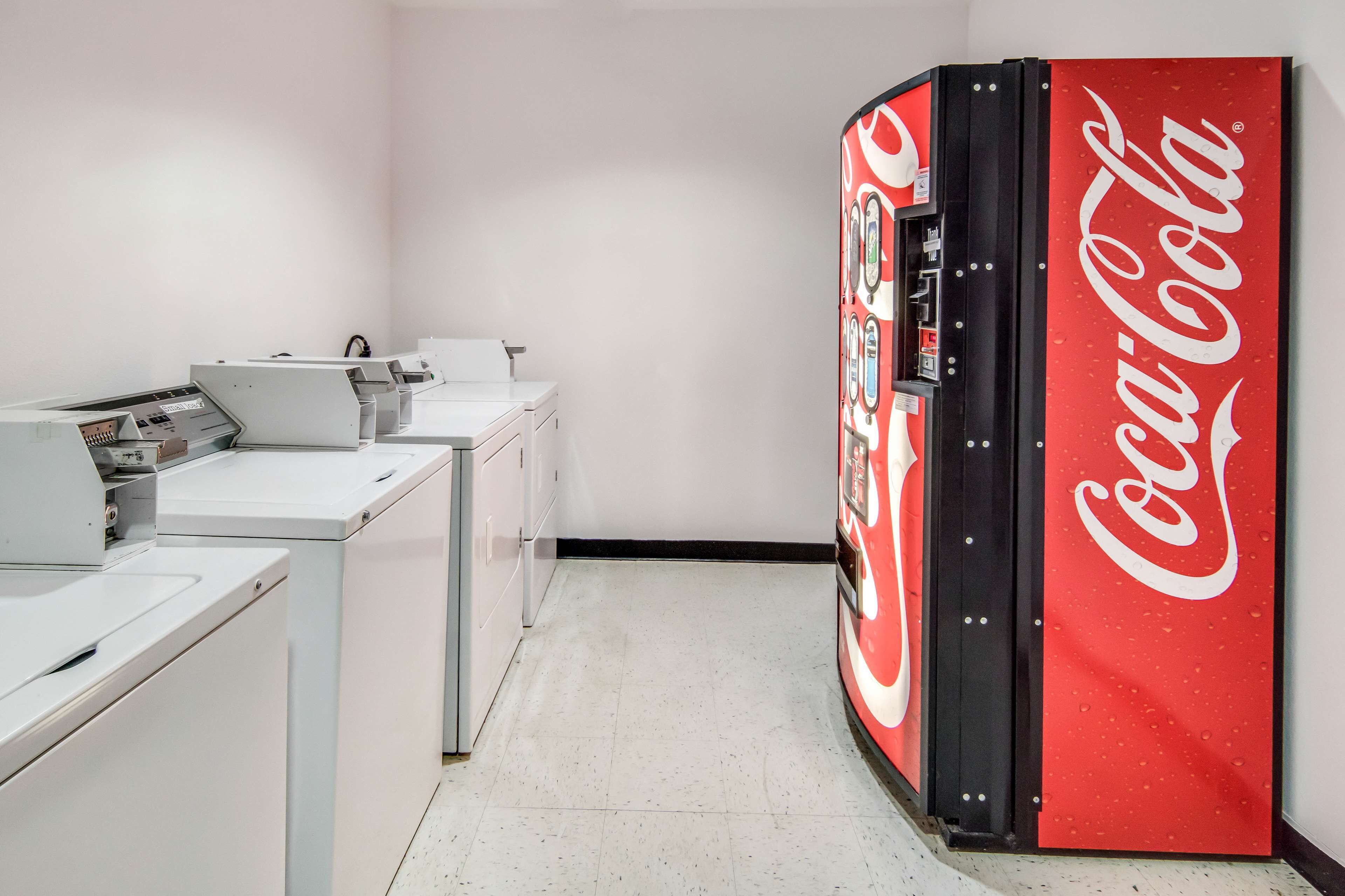 Un área de lavandería con lavadoras blancas y una máquina expendedora roja de Coca-Cola.