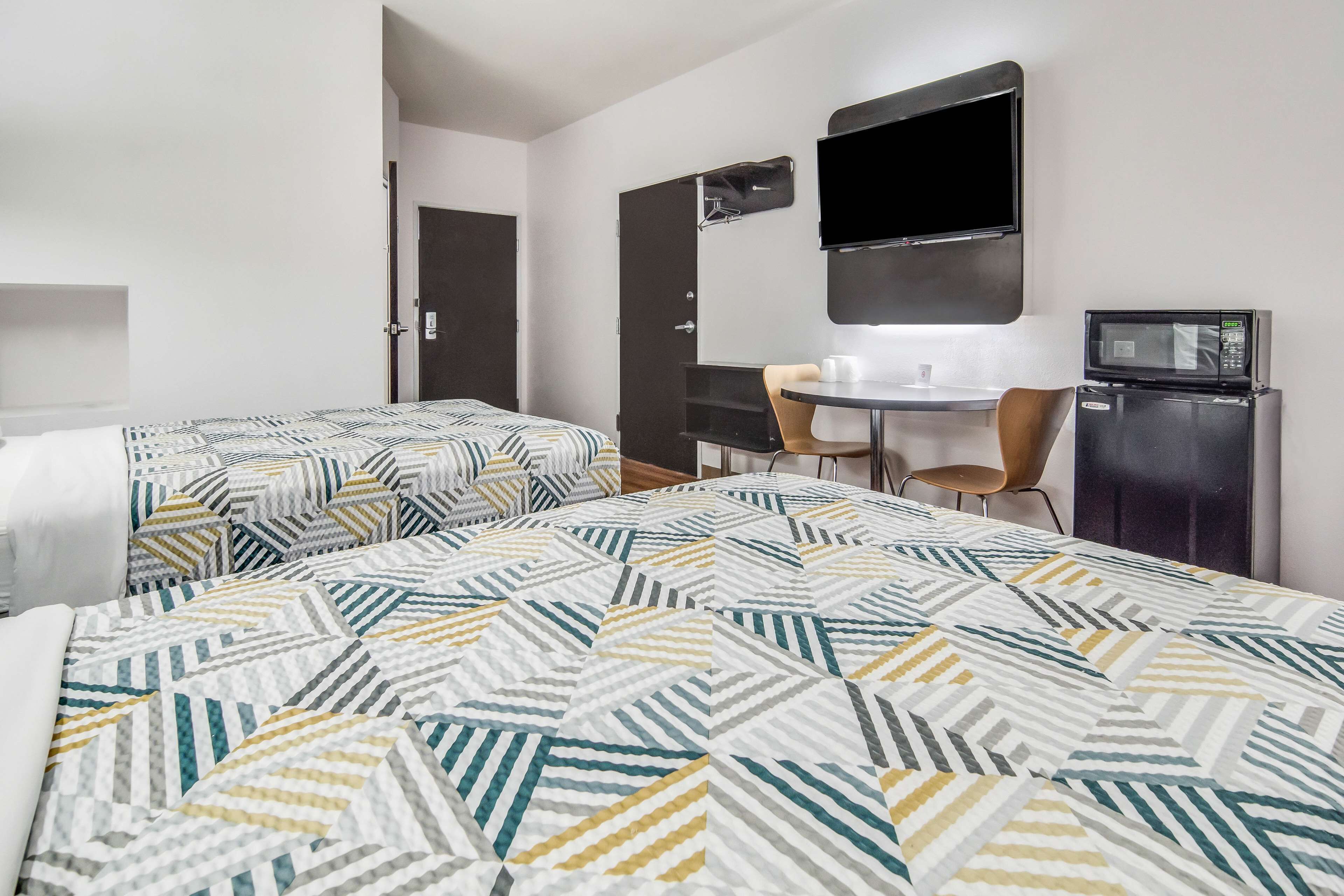 Habitación de hotel con dos camas, un escritorio, una silla, un televisor y un refrigerador.