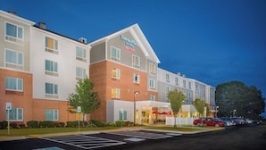 A TownePlace Suites hotel with a brick facade, multiple windows, and a parking lot with cars.
