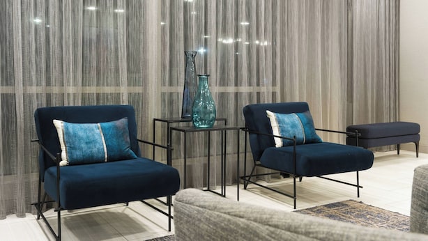 A modern living room with two dark blue armchairs, a small side table with a blue vase, and a bench.