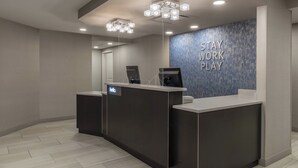 A reception area with a dark reception desk, a blue wall with the text "STAY WORK PLAY", and a modern light fixture above.