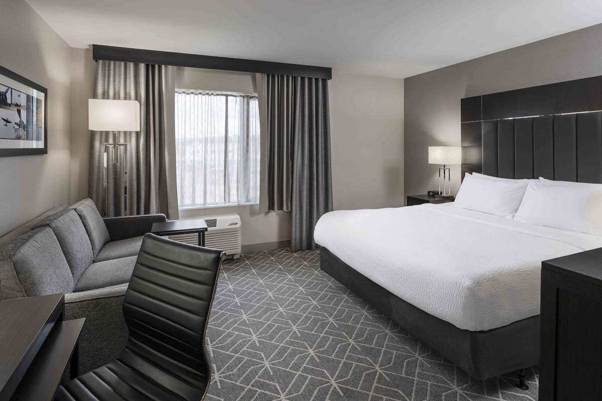 A hotel room with a large bed, a sofa, a desk, and a window with curtains.