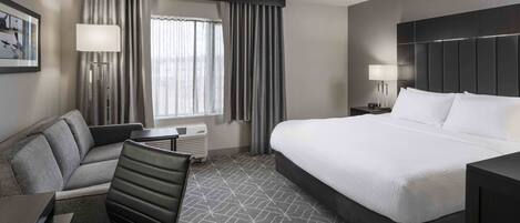Een hotelkamer met een groot bed, een bank, een bureau en een raam met gordijnen.