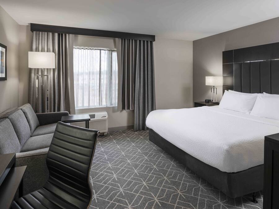 A hotel room with a large bed, a sofa, a desk, and a window with curtains.