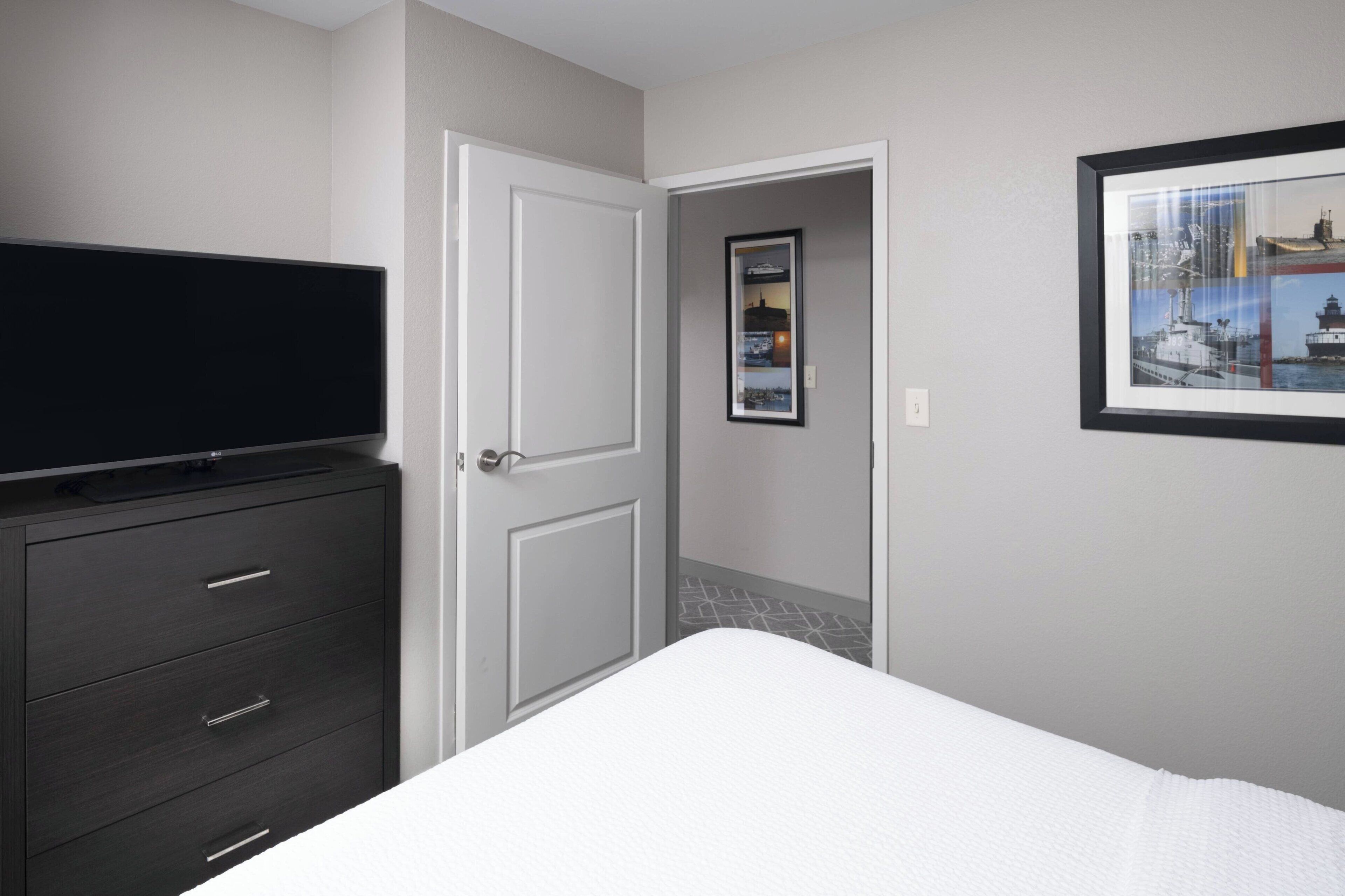 A bedroom with a bed, a dresser, a television, and a framed picture on the wall.