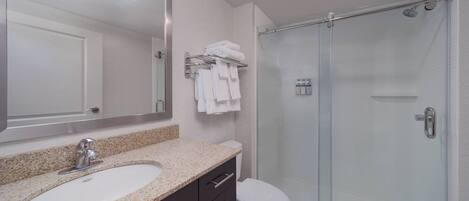 A modern bathroom with a granite countertop sink, a glass-enclosed shower, and a white toilet.