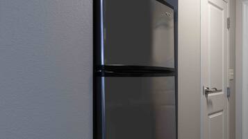 A black refrigerator in a room with white walls and a white door.