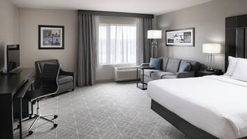 A hotel room with a large bed, a desk with a chair, a sofa, two wall-mounted lamps, and a window with curtains.