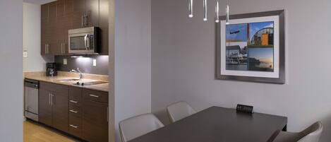 A modern kitchen with dark wooden cabinets, a built-in microwave, and a coffee maker. There is a dining area with a table and chairs, and a framed picture on the wall.