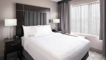 A hotel room with a large bed, two bedside tables with lamps, a modern headboard, and a large window with curtains.