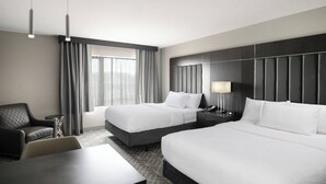 A hotel room with two beds, a desk, a chair, a lamp, and a view of the outdoors.