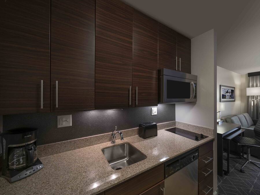 Una cocina moderna con gabinetes de madera oscura, un lavamanos de acero inoxidable, una cafetera y un microondas.