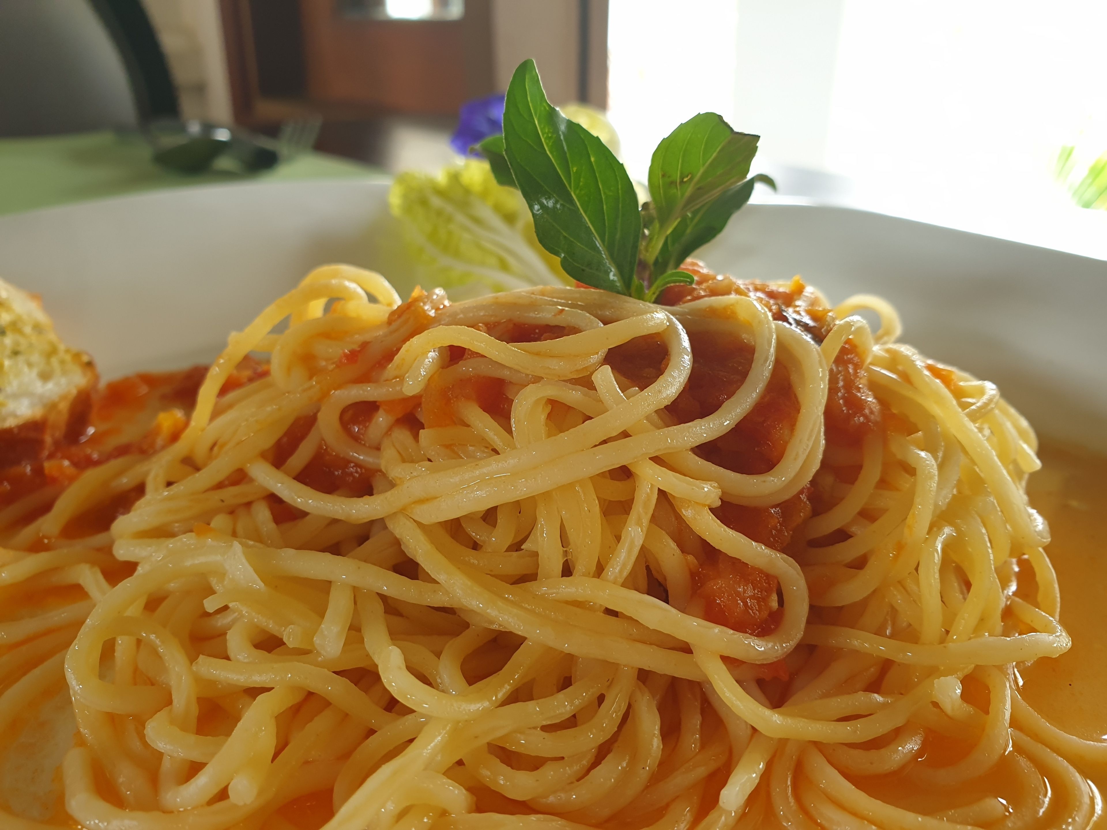 A plate of spaghetti with tomato sauce and a basil leaf garnish.