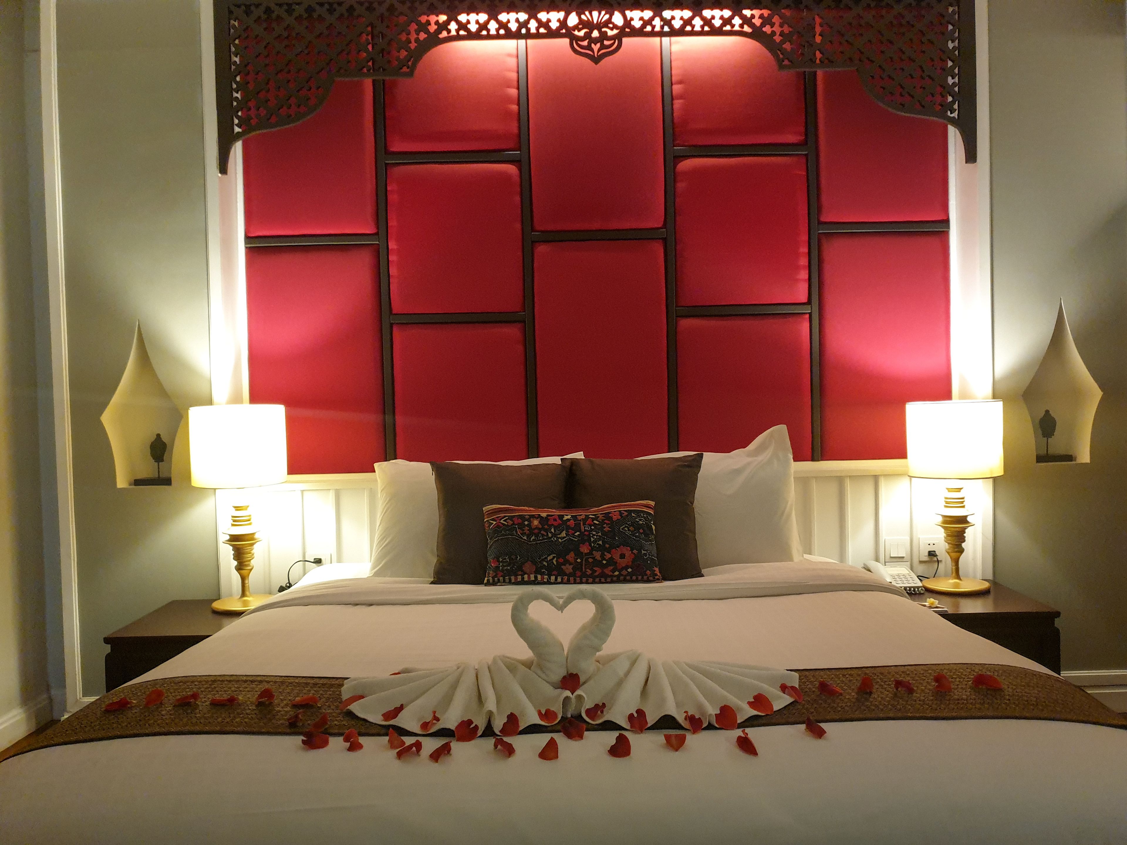 A hotel room with a large bed, red headboard, two bedside lamps, and a decorative swan made of towels on the bed.