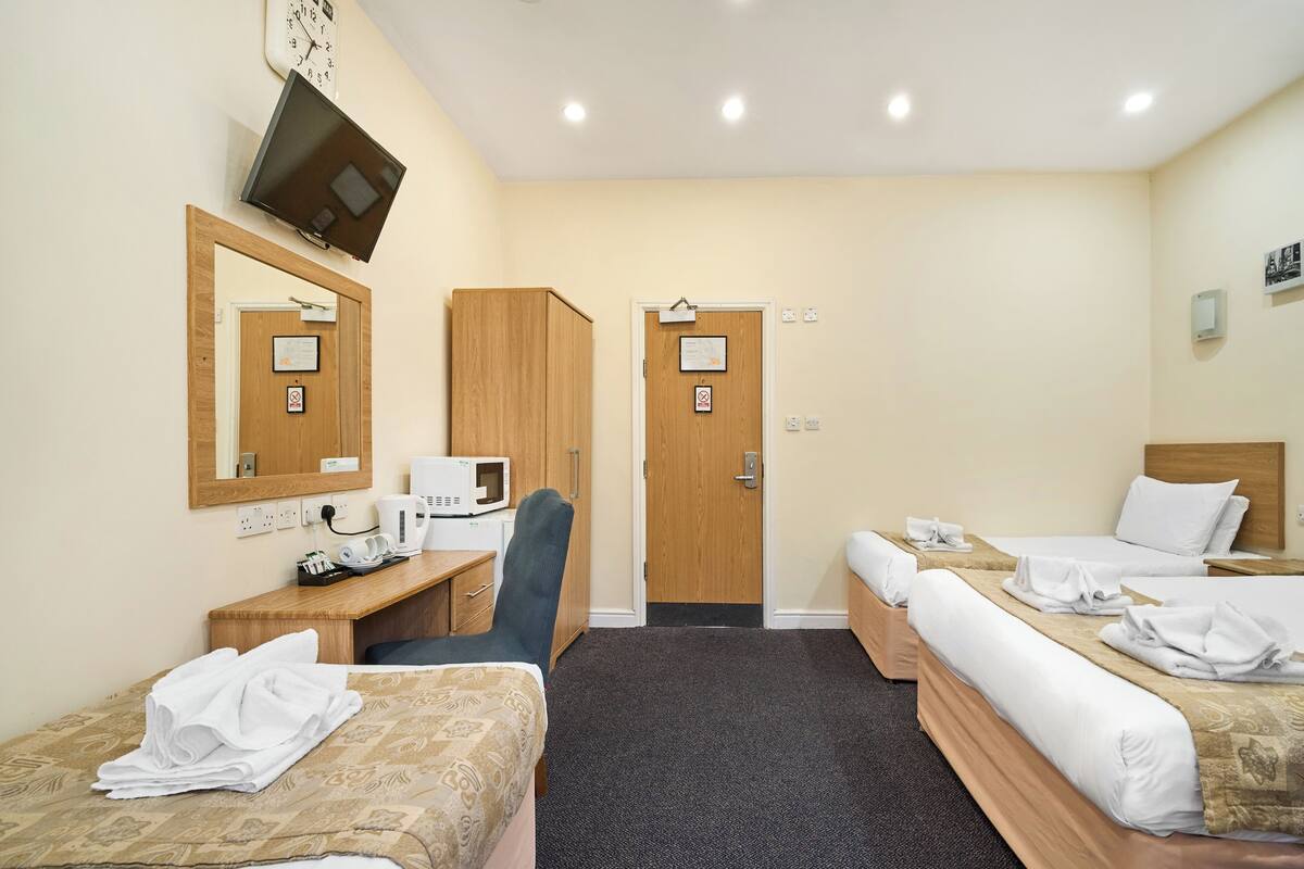 Habitación de hotel con dos camas, un escritorio, una silla, un televisor y un microondas.