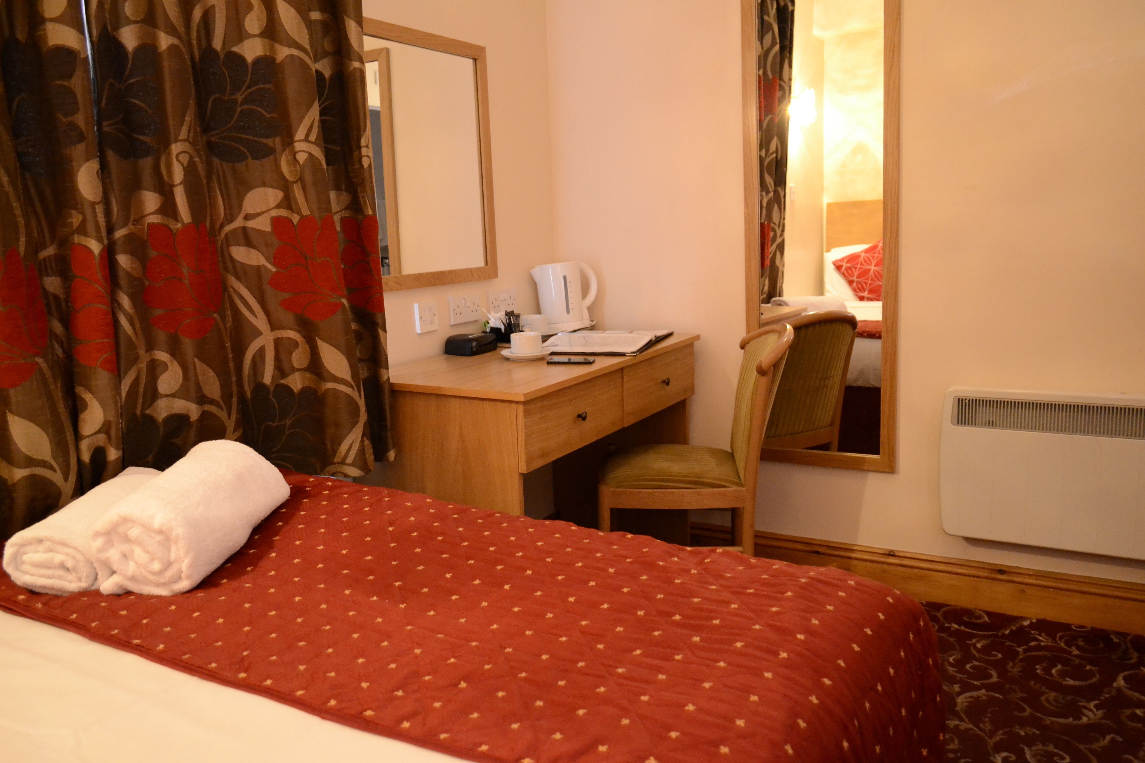 A hotel room with a bed, a desk, a chair, a mirror, and a window.