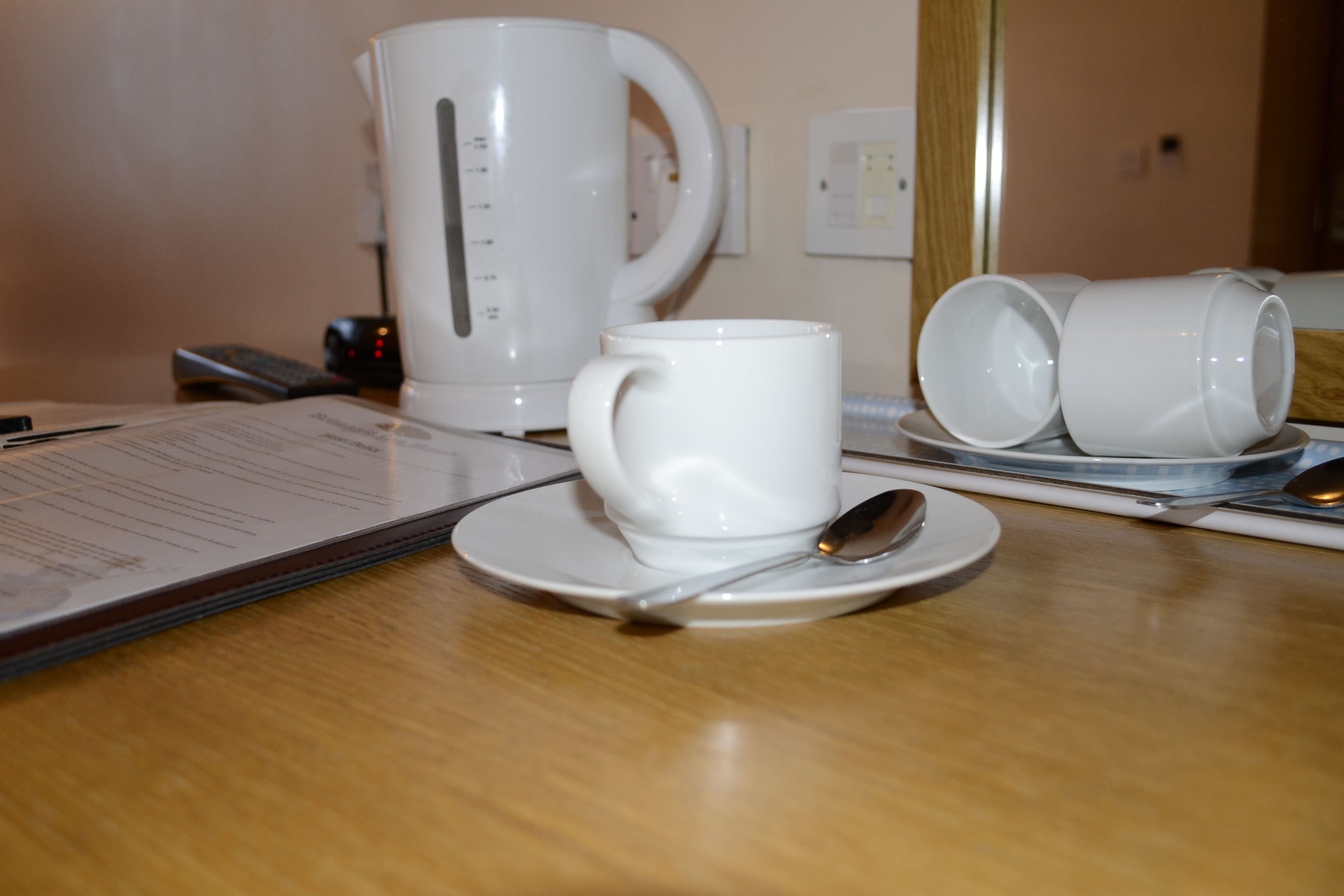 A table with a white coffee maker, a white mug, and two white cups on saucers, along with a spoon and a menu.